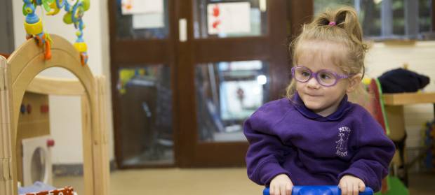 Small child wearing glasses and purple jumper sat in nursery